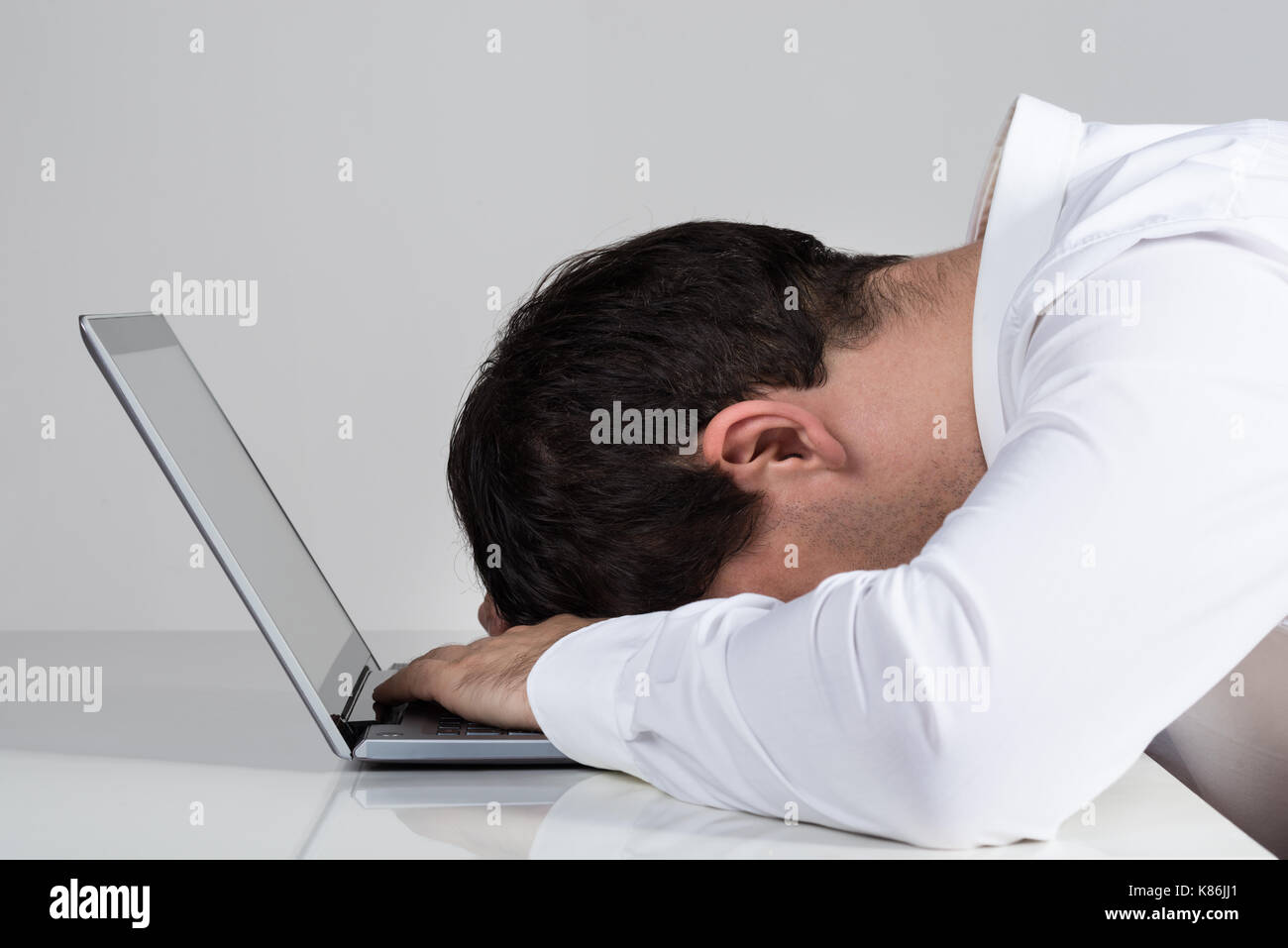 Vista laterale del sottolineato imprenditore appoggiata su laptop al banco contro uno sfondo bianco Foto Stock