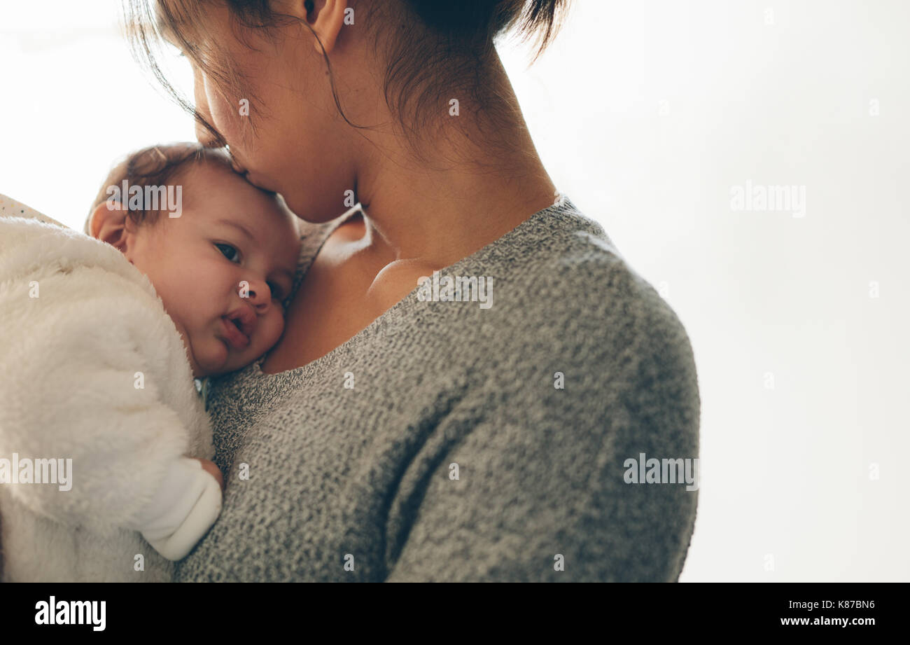 La donna che porta il figlio neonato e baciare sulla sua fronte. Carino piccolo Bambino fra le braccia della madre. Foto Stock
