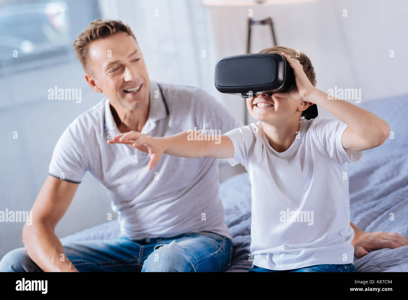 Padre orgoglioso guardando il suo felice boy prova auricolare vr Foto Stock