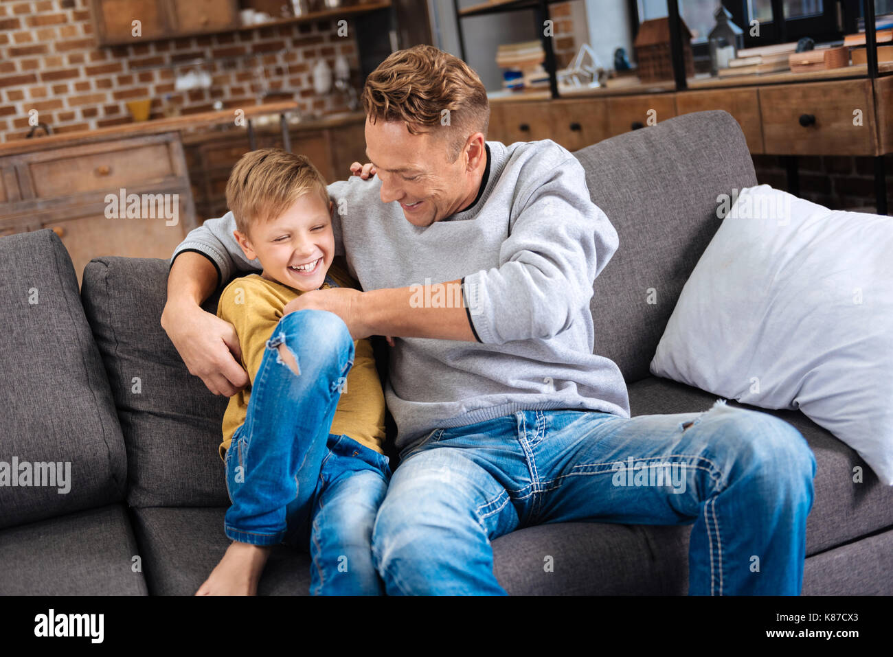 Padre amorevole solletico il suo piccolo figlio sul divano Foto Stock