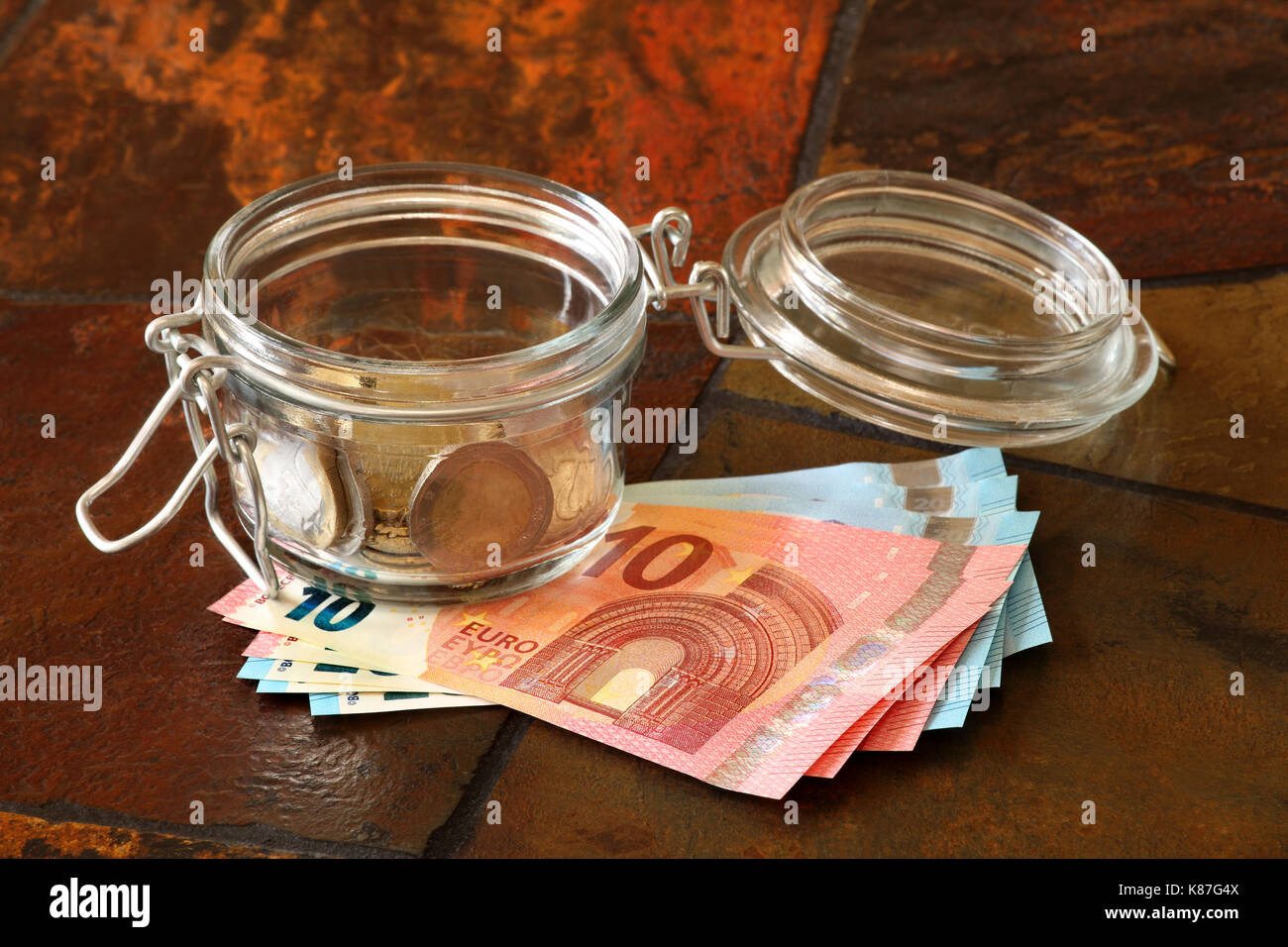 Monete metalliche in euro in un vaso con le banconote in euro al di sotto; mostrato su un tavolo piastrellato top Foto Stock
