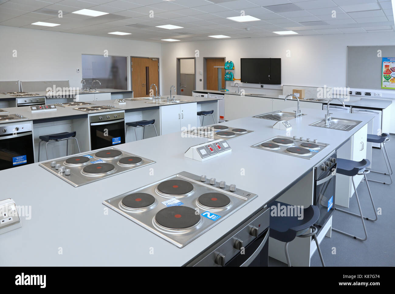 Economia domestica / classe di cucina in un nuovo, Londra scuola secondaria. Mostra piani di cottura e forni e insegnanti al di là del banco. Foto Stock
