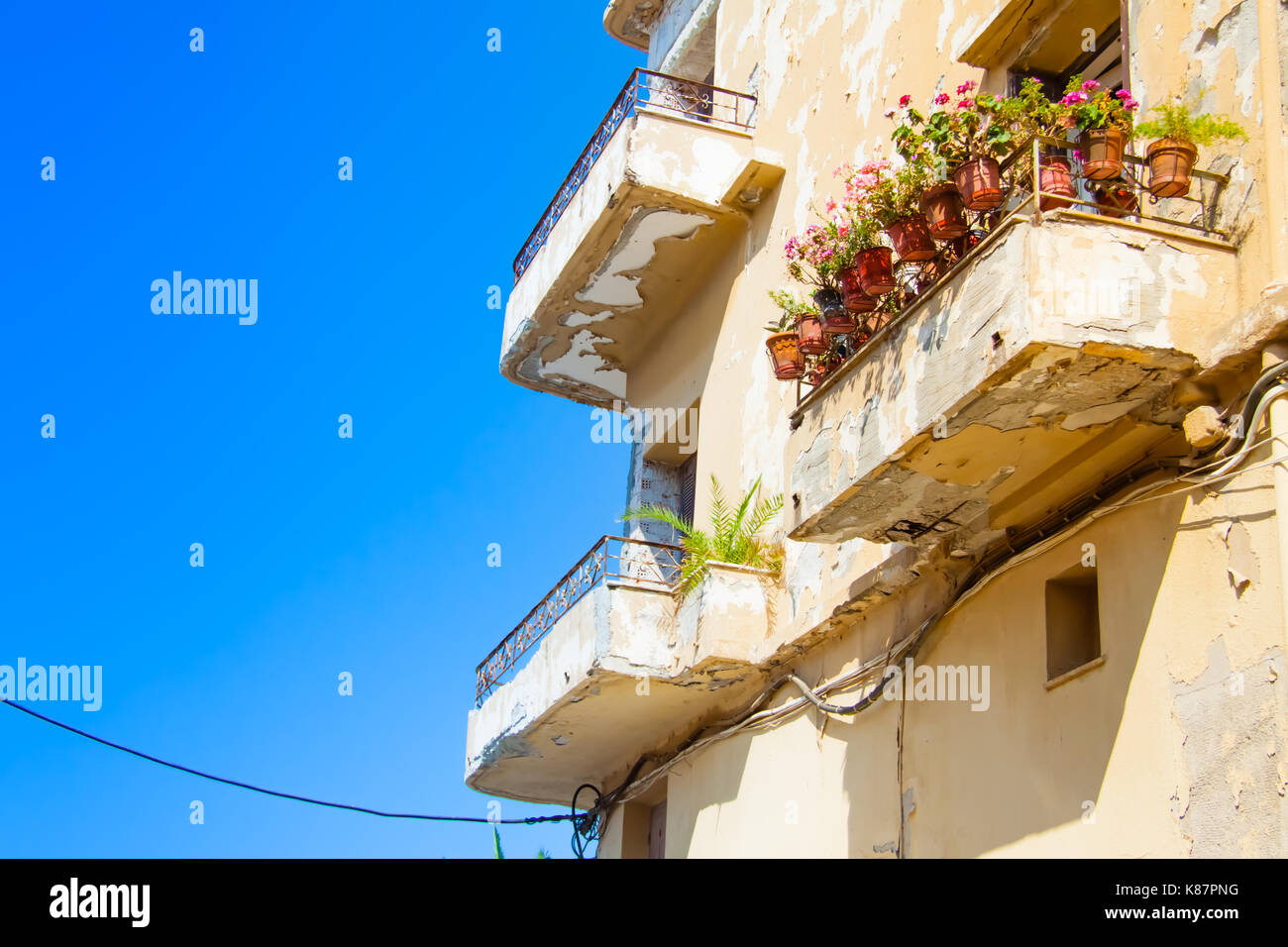 Malandato ma suggestivo balcone di un vecchio edificio decorato con fiori di colore rosa in vasi nella vecchia città di Rethimno, Creta, Grecia Foto Stock