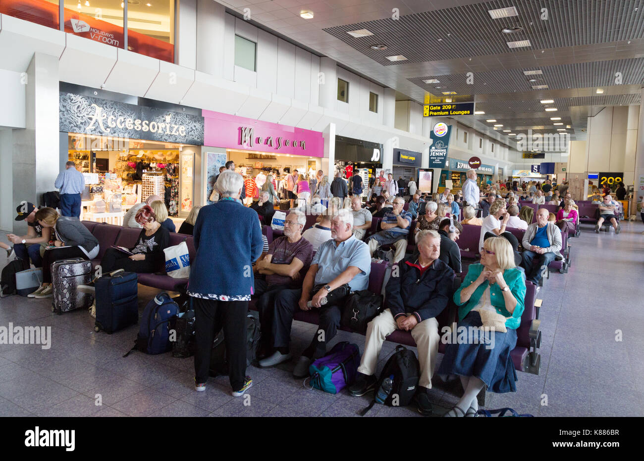 I passeggeri seduti nella sala partenze, terminale 2, aeroporto di Manchester, in Inghilterra, Regno Unito Foto Stock