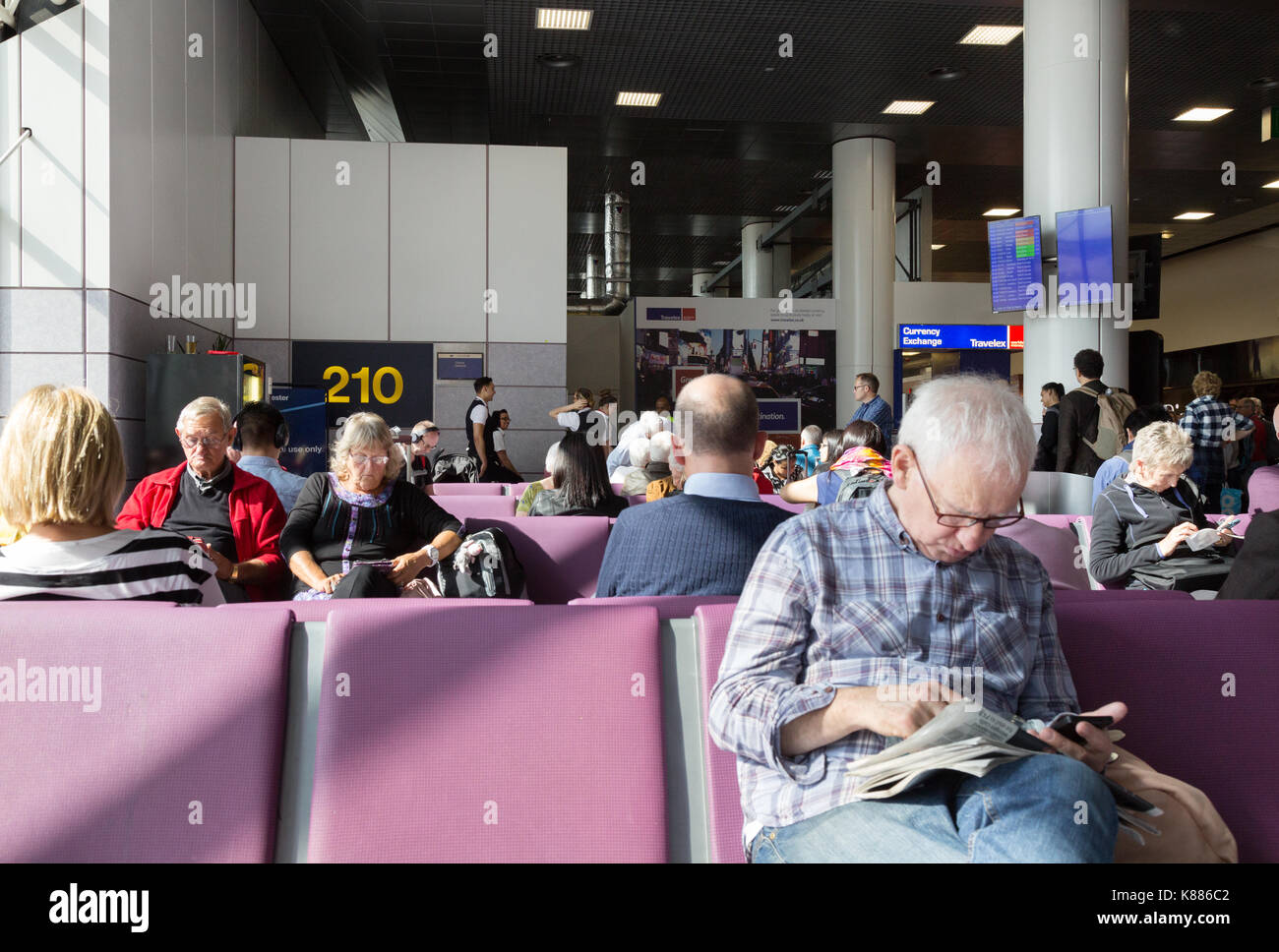 I passeggeri del trasporto aereo seduto alla porta, terminale 2, aeroporto di Manchester, Regno Unito Foto Stock