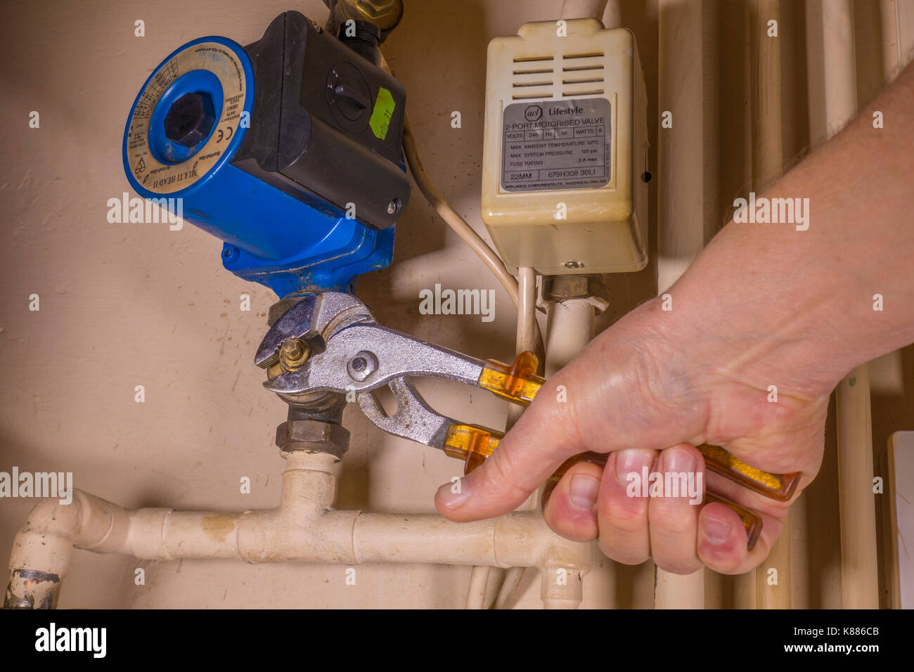 Un idraulico funzionante in un armadio di aerazione, utilizzando una chiave regolabile per lavorare su un difetto di riscaldamento centrale della pompa. Inghilterra, Regno Unito. Foto Stock