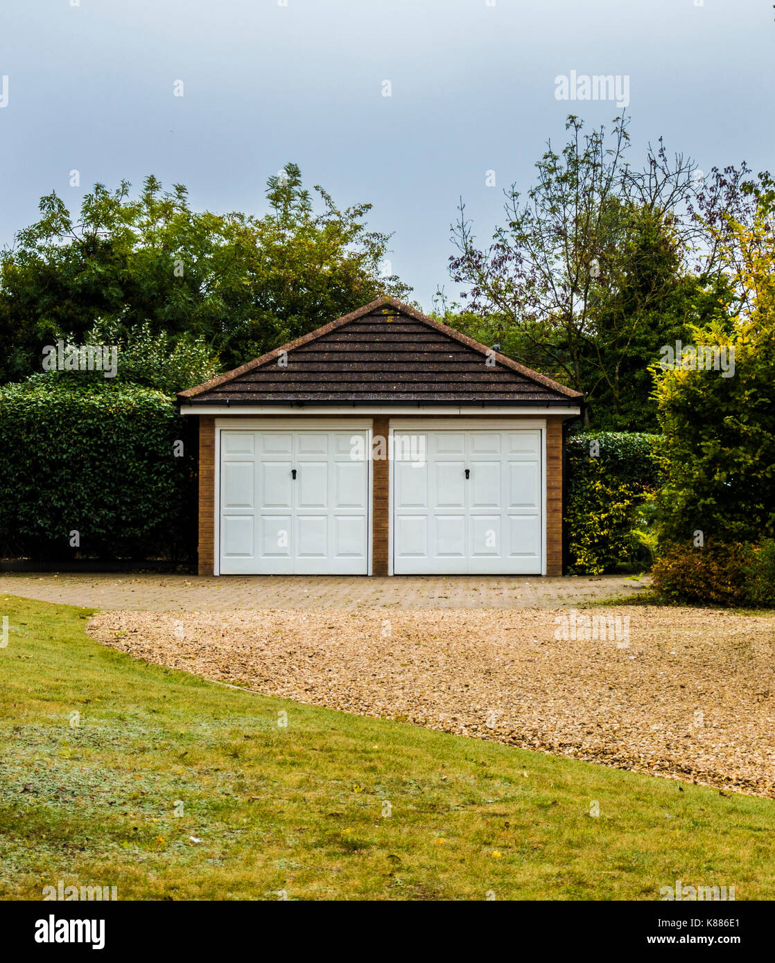 Moderno e spazioso, staccato doppio garage, con corrispondenti porte bianche e tetto a spiovente, su una unità di ghiaia, nel giardino di una casa in Inghilterra, Regno Unito. Foto Stock