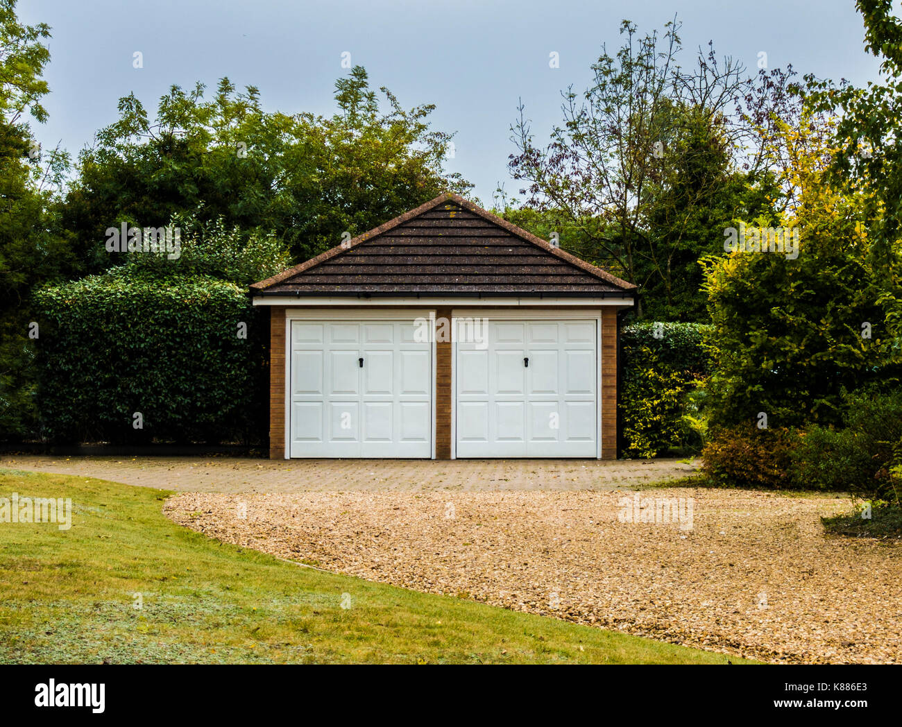 Moderno e spazioso, staccato doppio garage, con corrispondenti porte bianche e tetto a spiovente, su una unità di ghiaia, nel giardino di una casa in Inghilterra, Regno Unito. Foto Stock