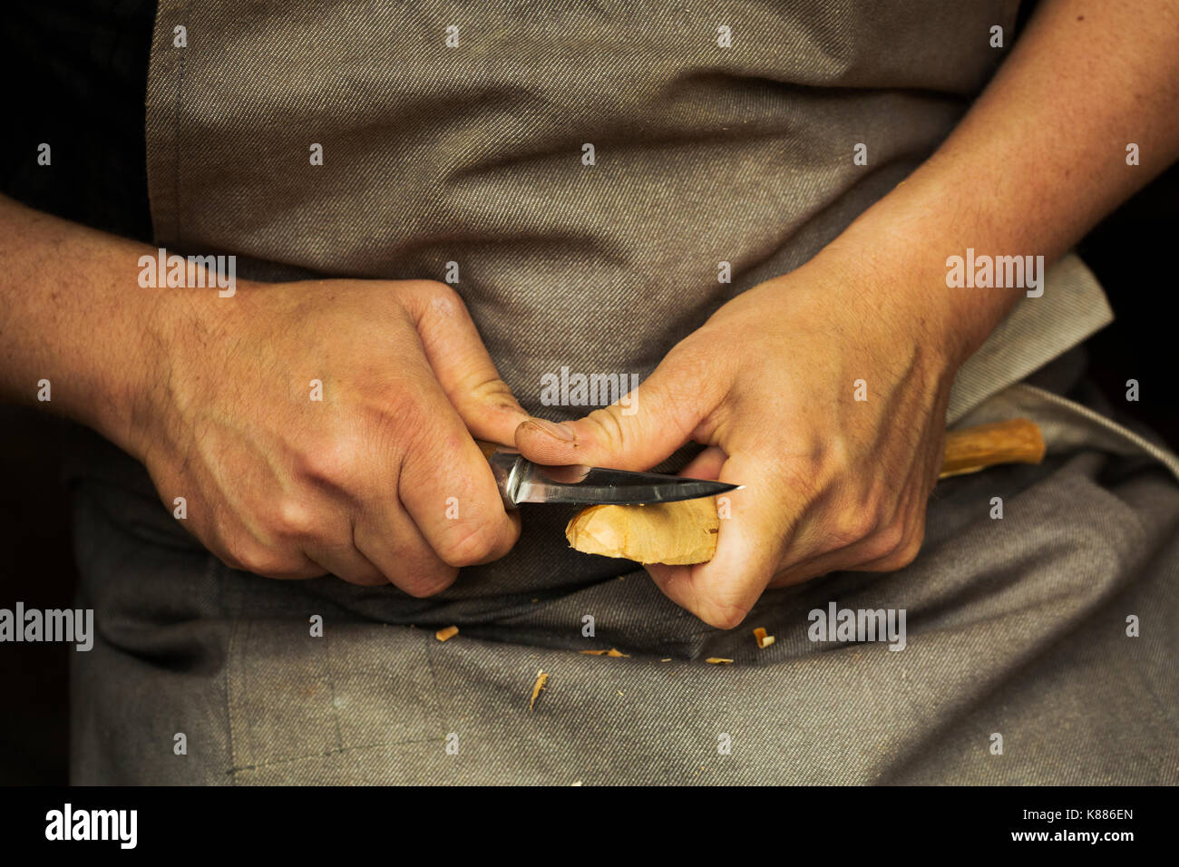 Close up di un artigiano di mani premendo e sagomatura di un piccolo pezzo di legno in un cucchiaio con una lama affilata lama, sagomando la ciotola all'indietro. Foto Stock