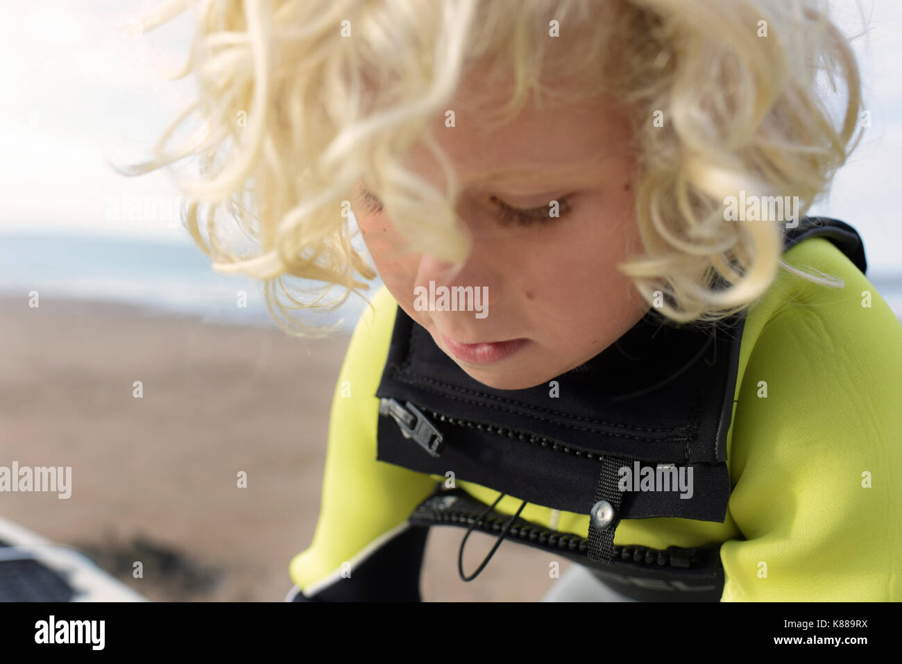 Giovane ragazzo sempre pronto a navigare con la sua tavola da surf in spiaggia indossando una muta su una giornata d'estate. Foto Stock
