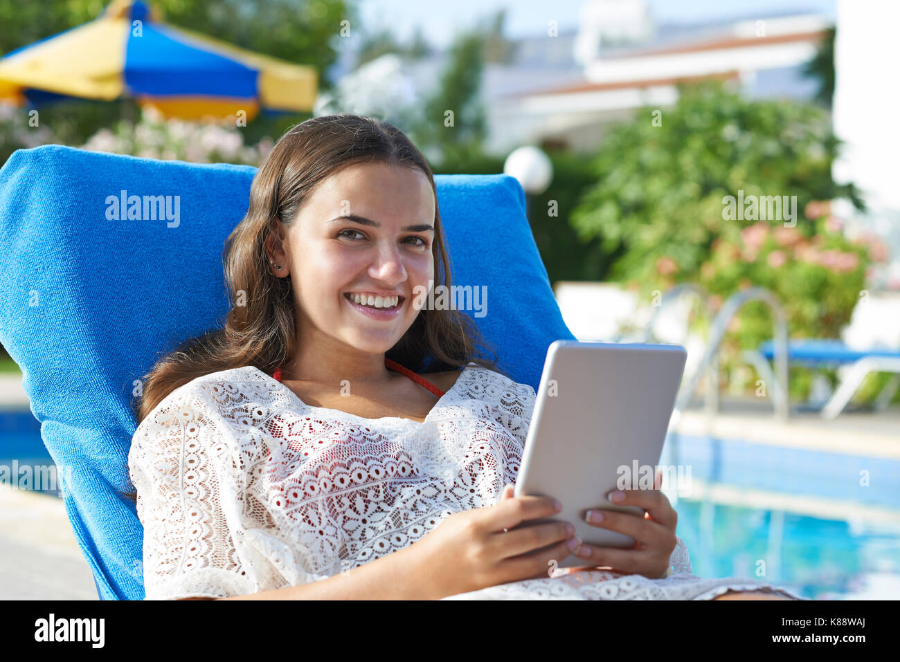 Ragazza giovane con tavoletta digitale mentre vi rilassate in piscina in vacanza Foto Stock