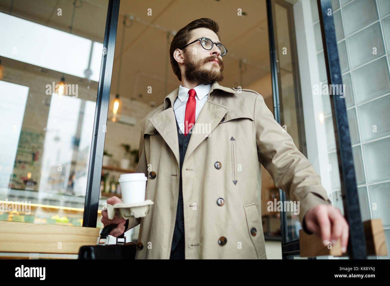 Ben vestito uomo barbuto con vetro di caffè andando fuori del caffè dopo pranzo Foto Stock
