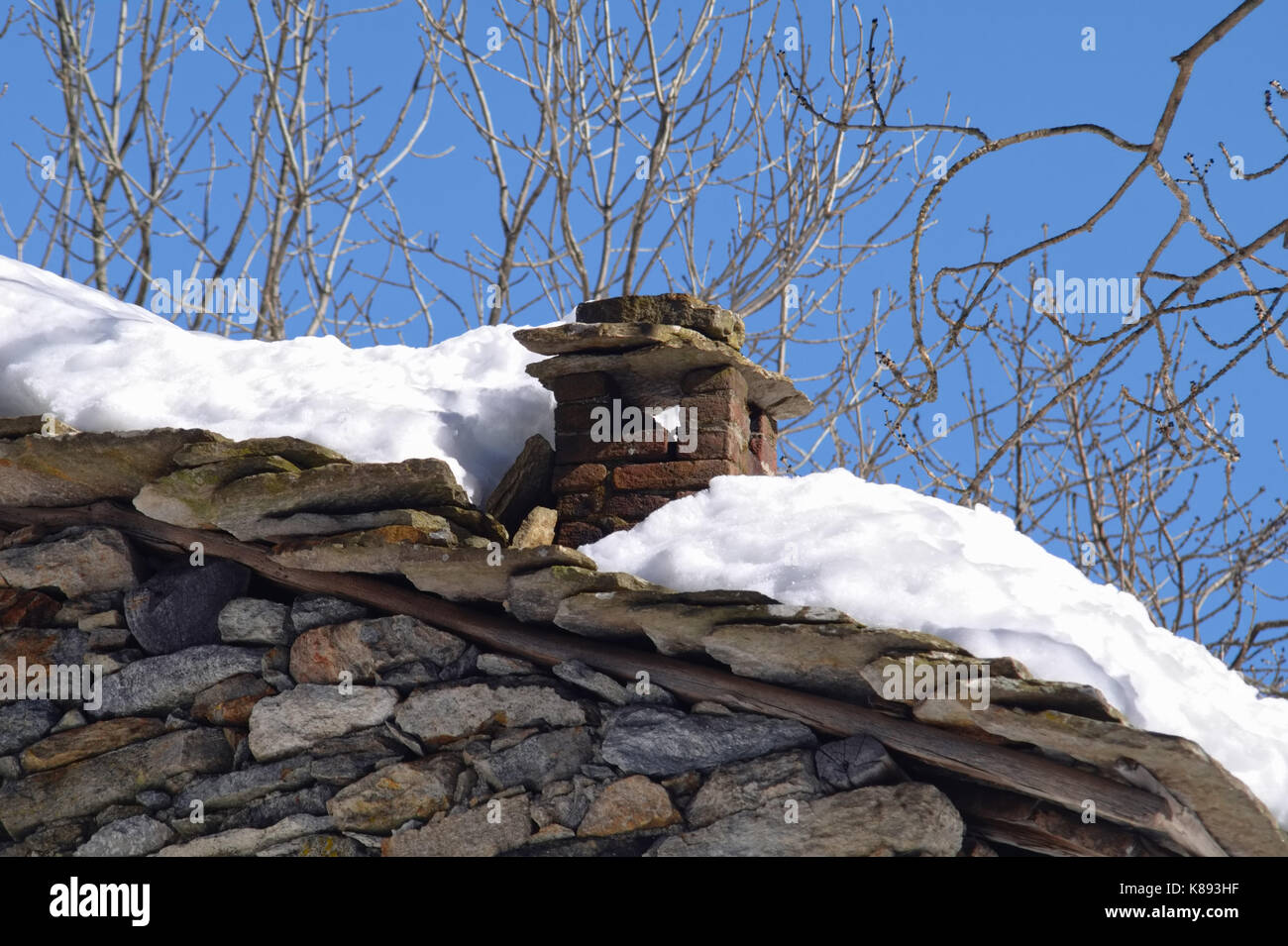 Vecchio camino innevato con il cielo azzurro e gli alberi in background, il fuoco selettivo sulla costruzione Foto Stock
