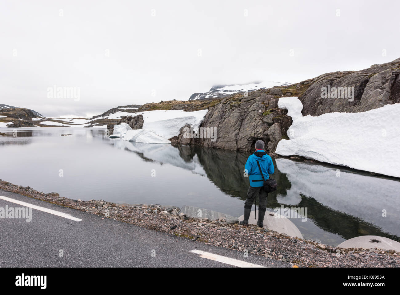 Fotografo tenendo la foto del tipico paesaggio norvegese con montagne innevate e chiaro lago vicino la famosa montagna aurlandsvegen road, aurland, né Foto Stock