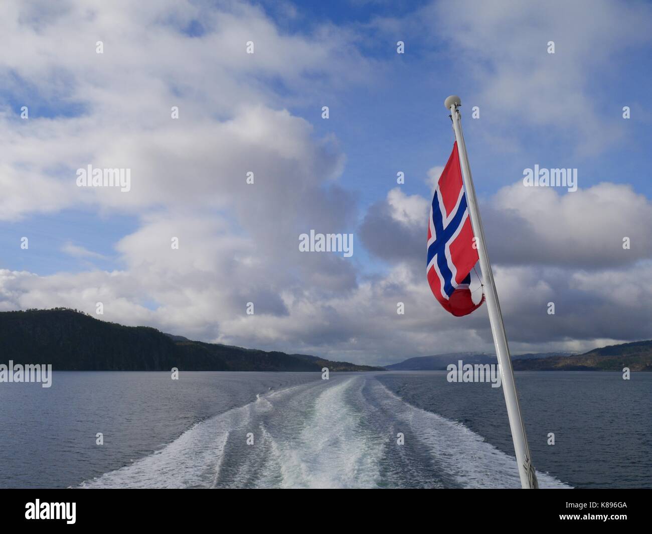 La bandiera norvegese vola sulla scia di un catamarano sul fiordo, Osterfjorden, Norvegia Foto Stock