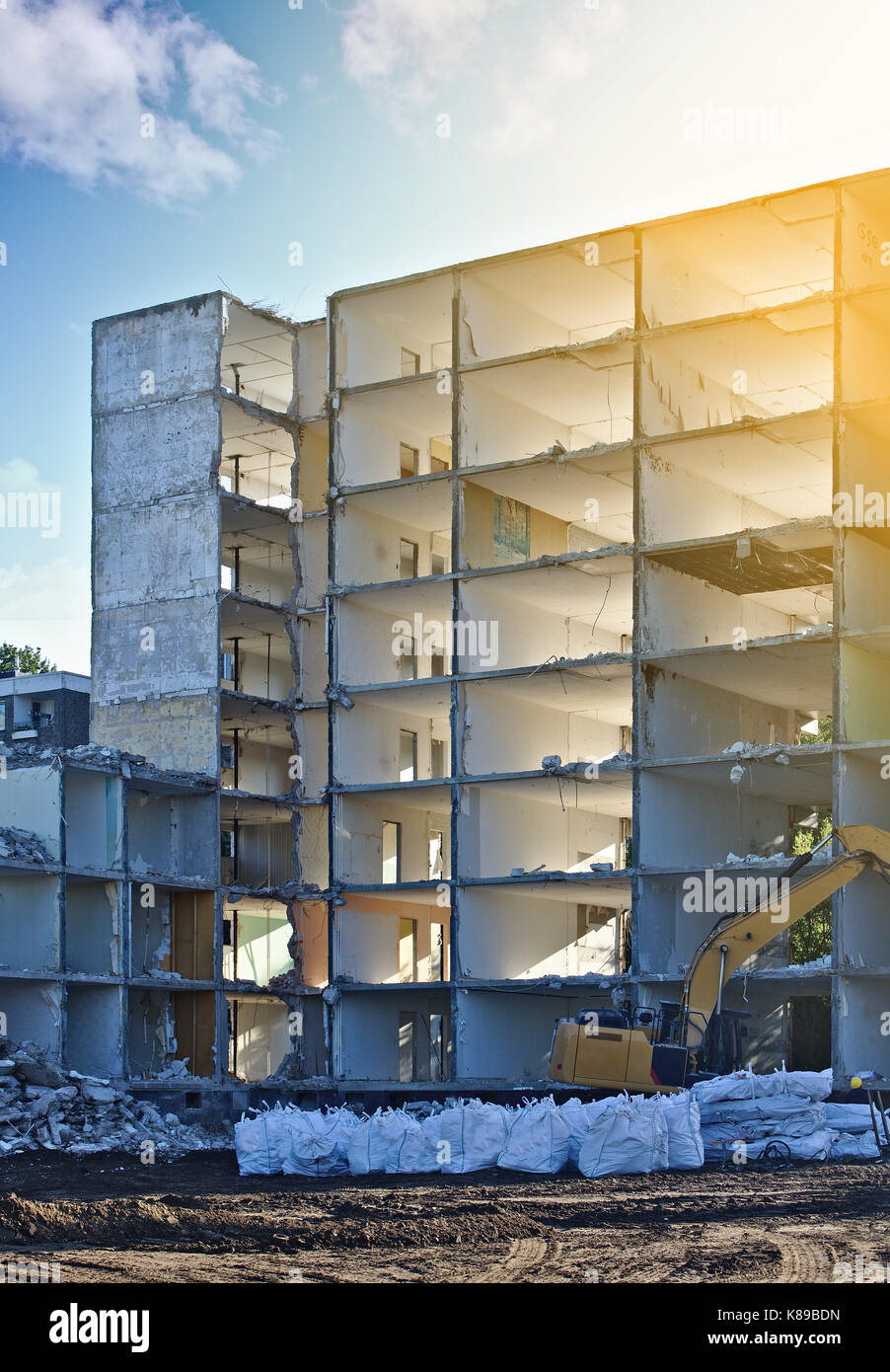 Demolito palazzo residenziale con escavatore ed enormi sacchetti di plastica riempiti con pietrisco in primo piano Foto Stock
