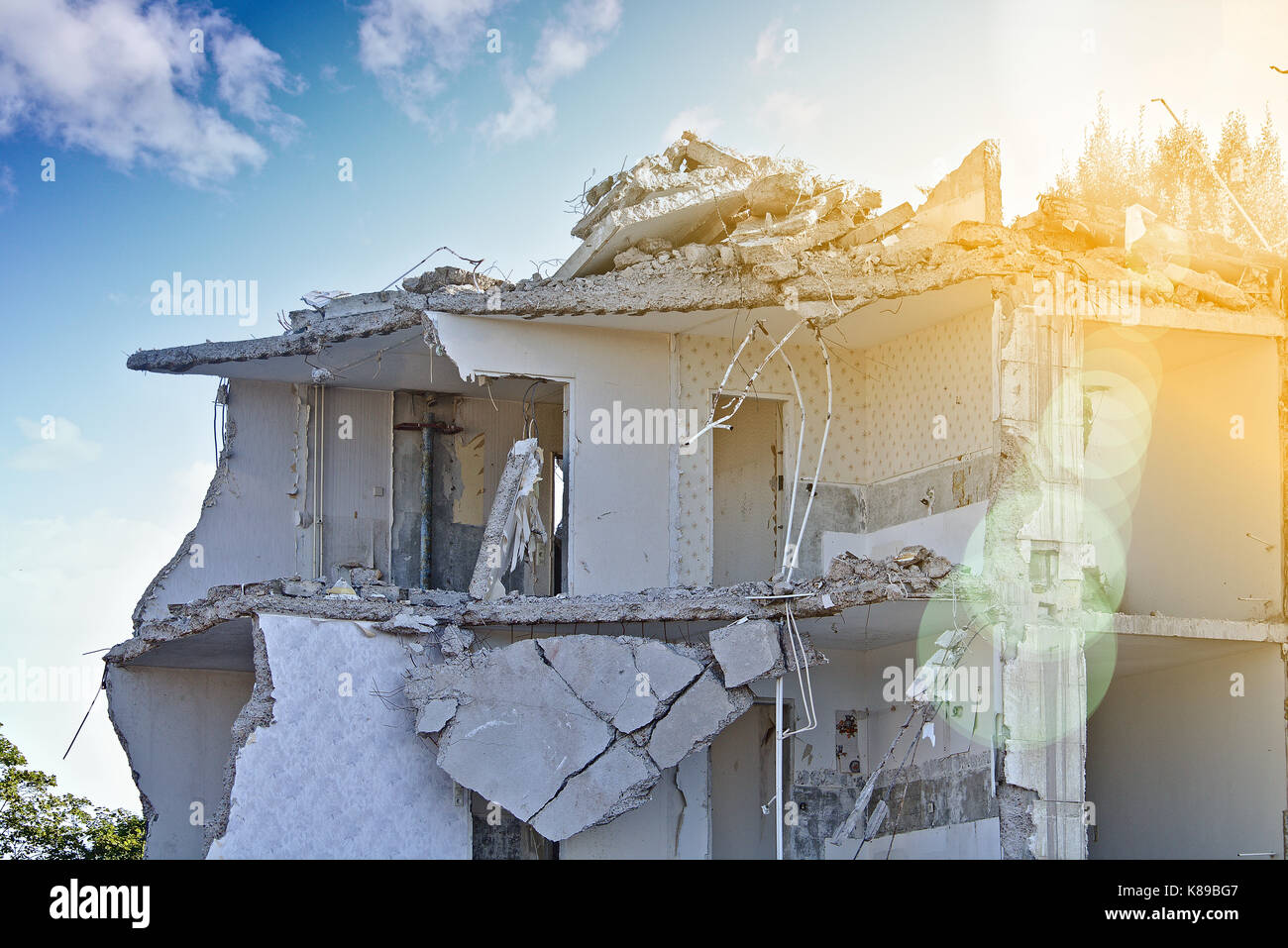La rovina di un parzialmente demolito palazzo residenziale (piano superiore) davanti a un cielo blu con nuvole bianche, soleggiato con lens flare Foto Stock