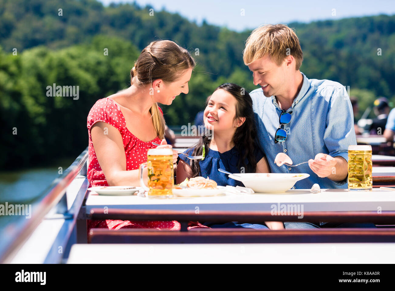 La famiglia a pranzo sulla crociera fluviale con bicchieri da birra sul ponte Foto Stock