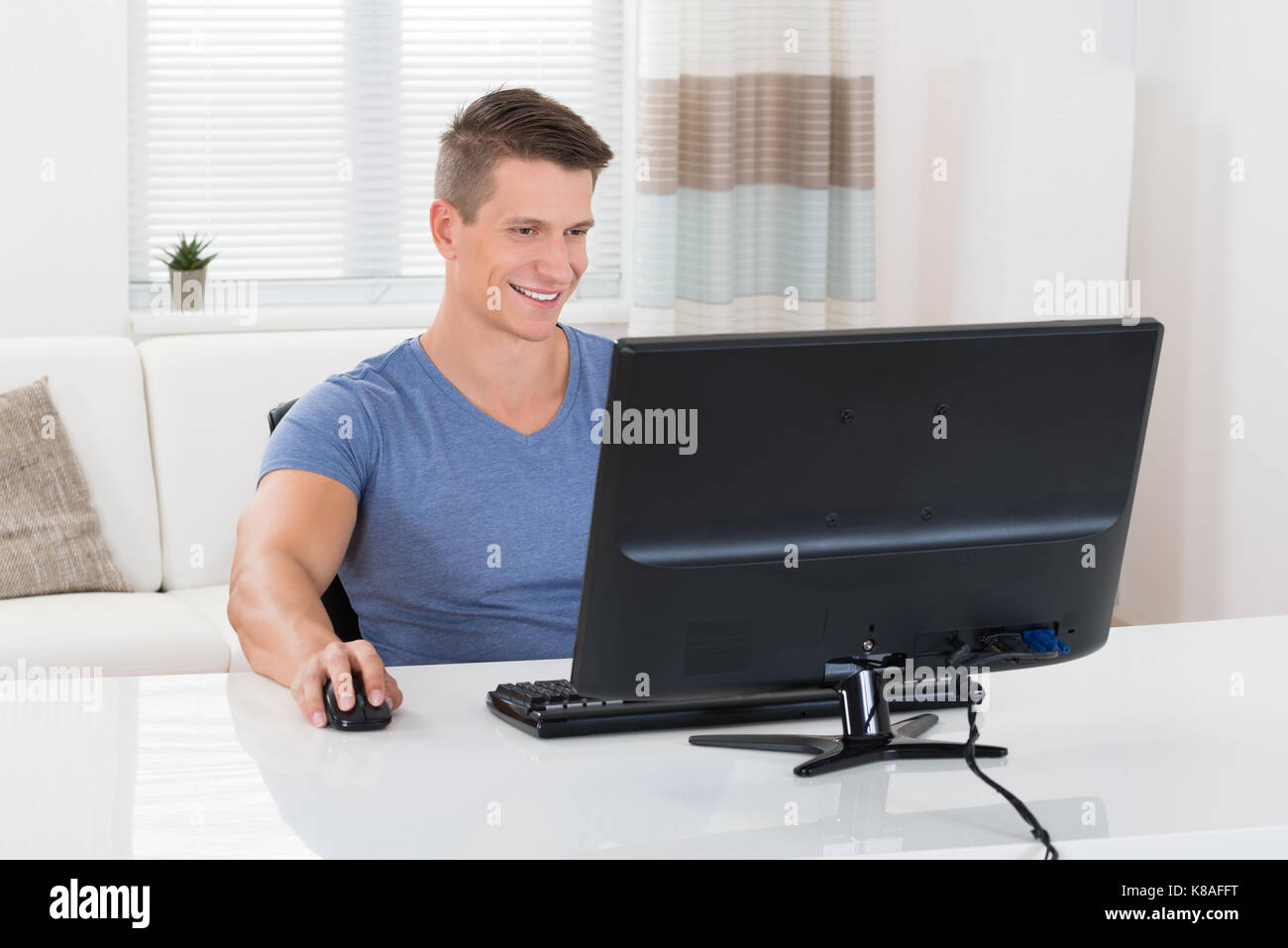 Giovane uomo felice utilizzando il computer desktop nel soggiorno Foto Stock