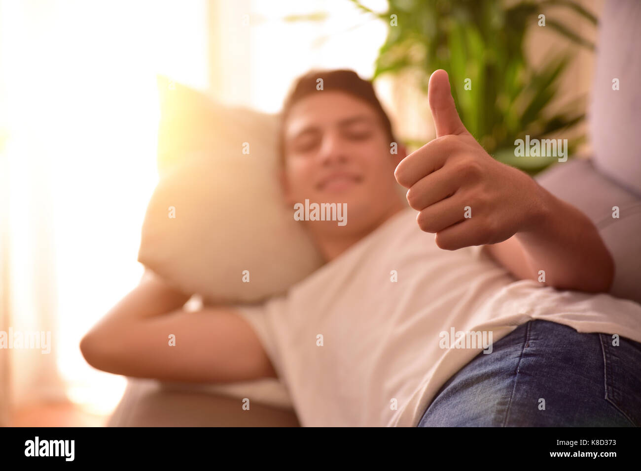 Teenage giacente su un divano di casa facendo il segno OK con la sua mano. Concetto di riposo e comfort Foto Stock