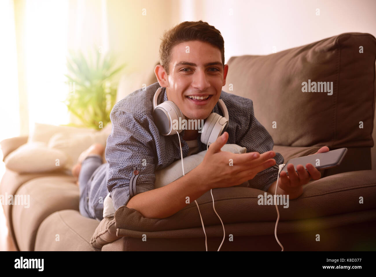 Teen ascoltando musica con le cuffie da mobile sdraiato a faccia in giù sul lettino sorpreso e ridere Foto Stock