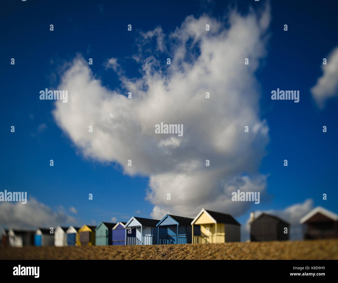 Un enorme nuvola bianca contro un cielo blu torreggia su una fila di pittoresca spiaggia di capanne a Calshot Hampshire Inghilterra Foto Stock