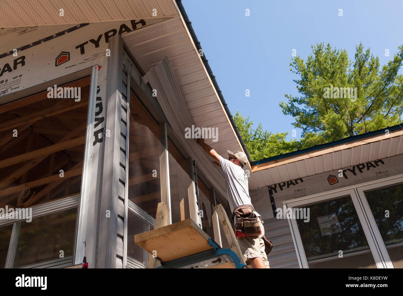Un lavoratore edile installando un pezzo di rivestimento di vinile su una impalcatura temporanea in Ontario, Canada. Foto Stock