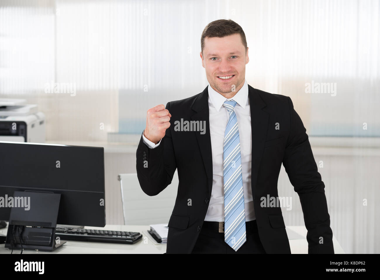 Ritratto di imprenditore di successo clenching pugno mentre permanente al computer scrivania in ufficio Foto Stock