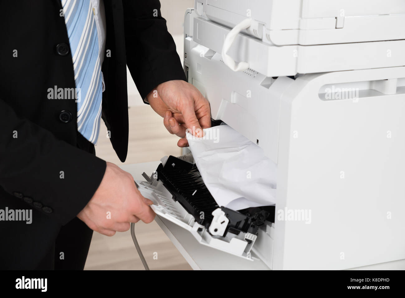 Immagine ritagliata di imprenditore di rimuovere la carta bloccata nella stampante in ufficio Foto Stock