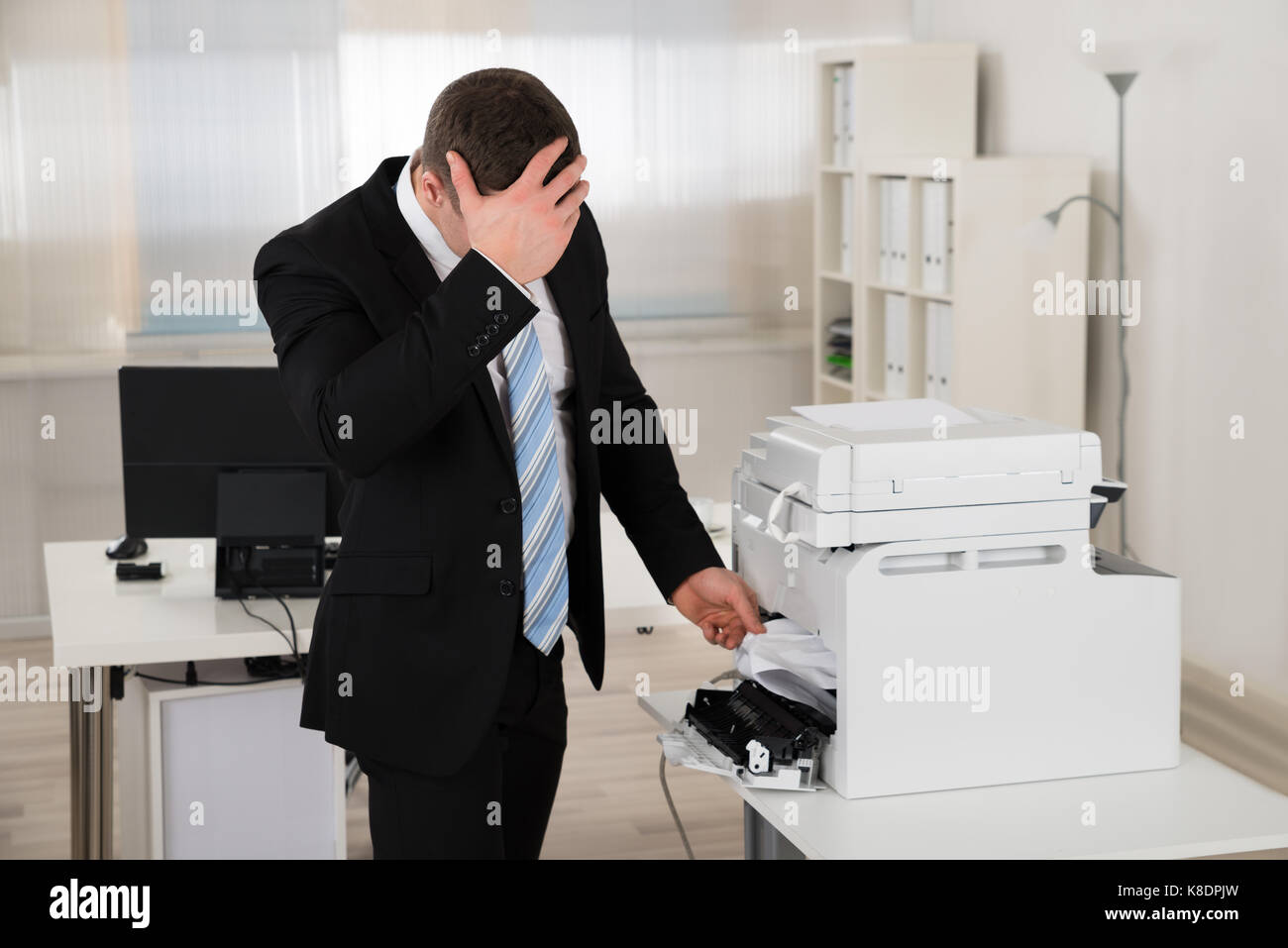 Imprenditore irritata guardando la carta bloccata nella stampante in ufficio Foto Stock