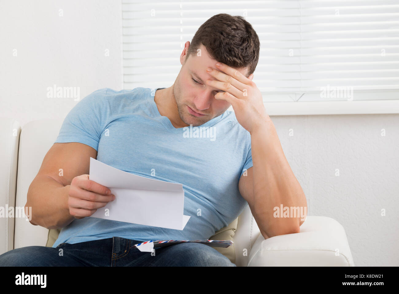 Sconvolto metà uomo adulto con testa in mano la lettera di lettura sul divano di casa Foto Stock