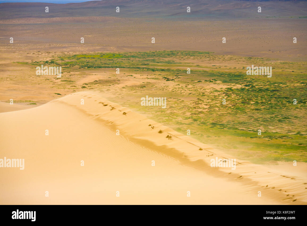 Vento che soffia granelli di sabbia a partire dal bordo superiore della Khongor Els Dune di sabbia nel deserto del Gobi in Mongolia Foto Stock