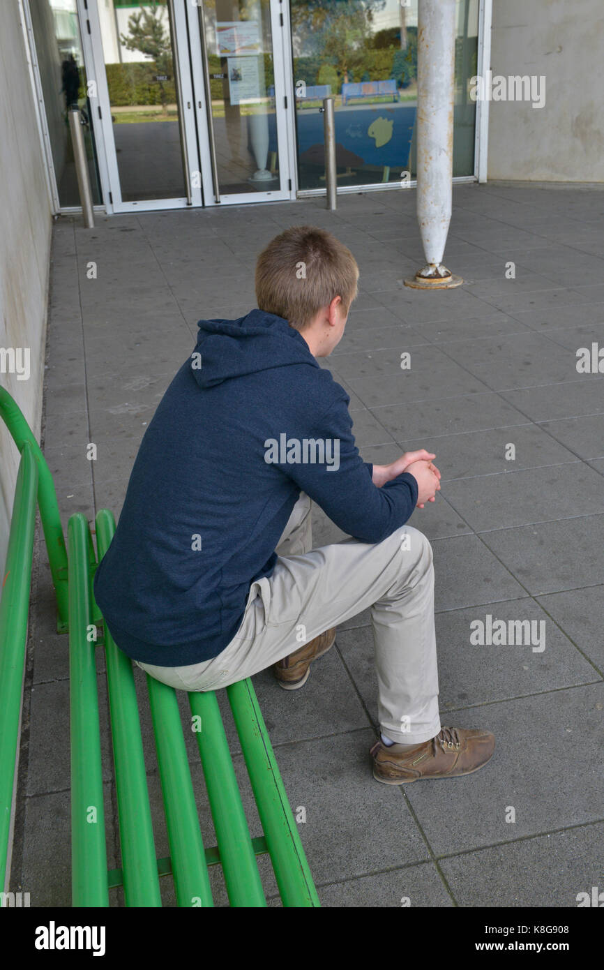Far cadere al di fuori della scuola. Alta scuola studente seduto su una panchina all'ingresso della high school.Caption locale *** Foto Stock