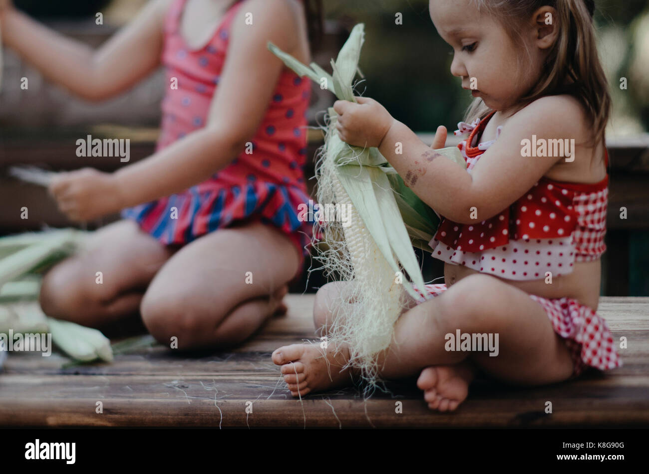 Sorelle rimozione Corn buccia mentre è seduto sul banco di lavoro Foto Stock