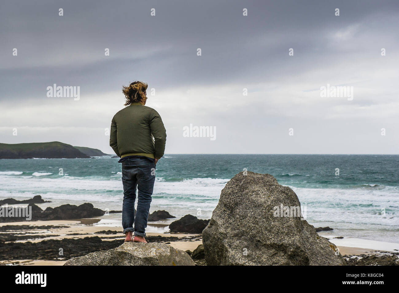 Newquay Cornwall - un uomo a piedi nudi in piedi su una roccia che si affaccia poco fistral in Newquay, Cornwall. Foto Stock