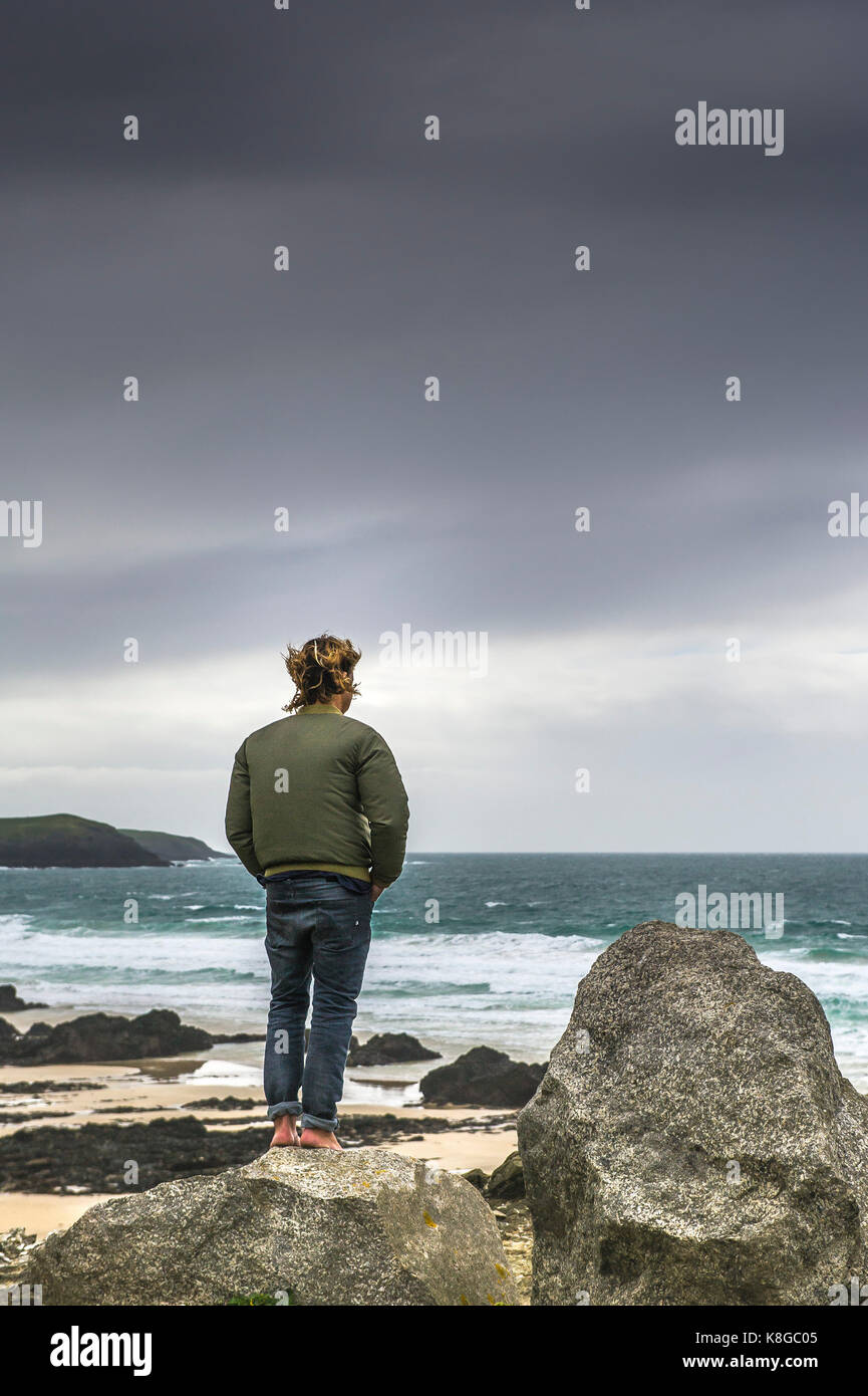 Newquay Cornwall - un uomo a piedi nudi in piedi su una roccia che si affaccia poco fistral in Newquay, Cornwall. Foto Stock