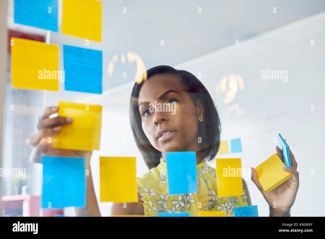 Giovane donna in ufficio, incollaggio note adesive per vetro in ufficio Foto Stock