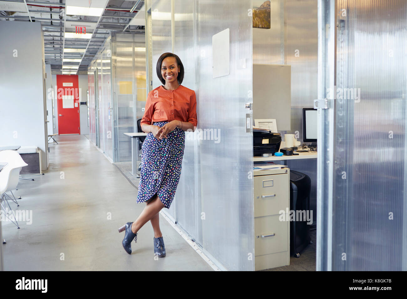 Ritratto di imprenditrice in piedi nel corridoio di office, appoggiata contro office surround, sorridente Foto Stock