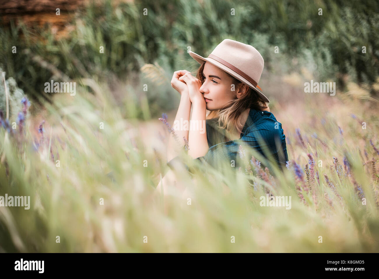 Metà donna adulta seduta in erba lunga, riflessivo espressioni Foto Stock