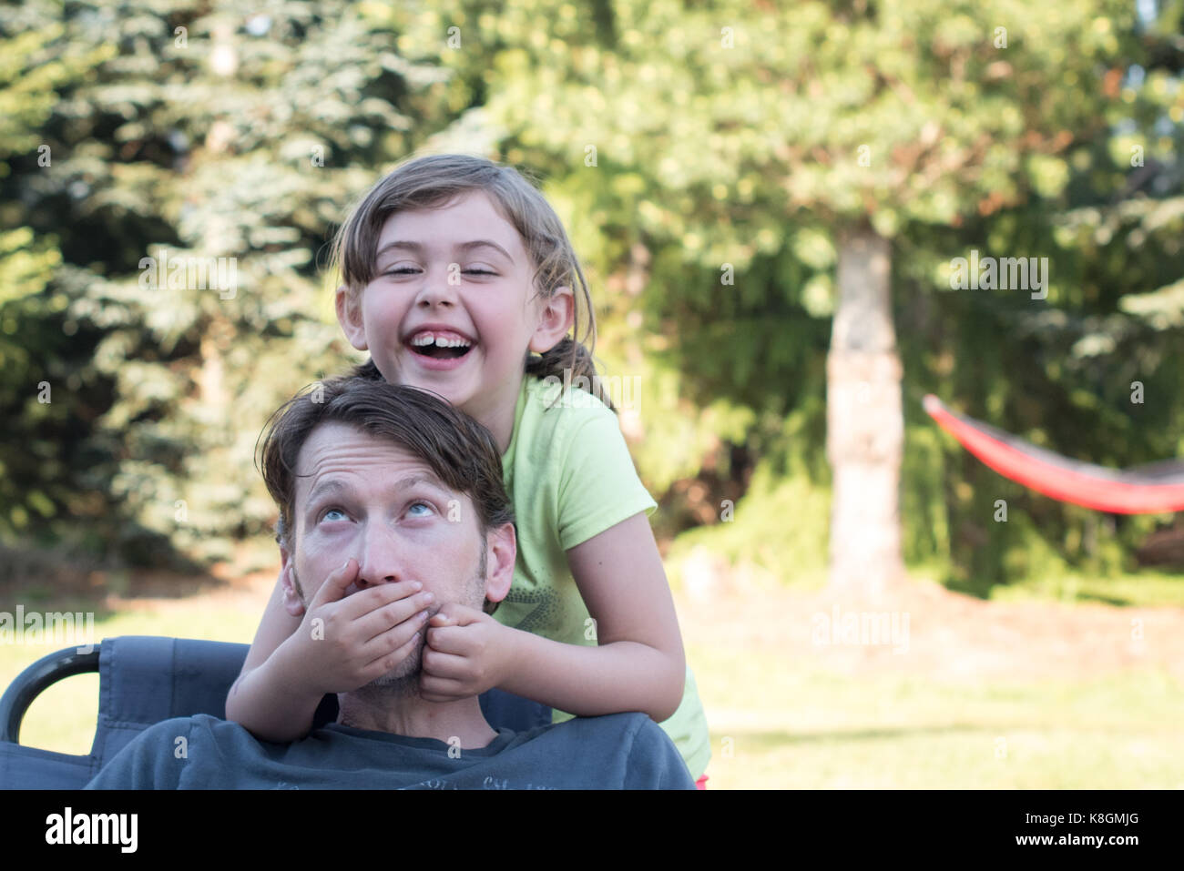 Padre e figlia ingannare intorno all'aperto, ragazza giovane padre che copre la bocca, ridendo Foto Stock
