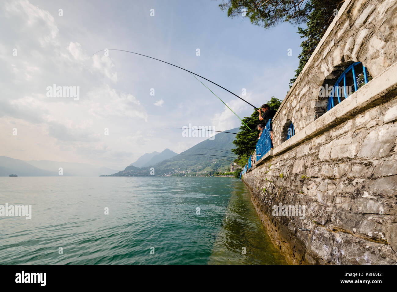 Il pescatore mit langen angelruten an der Mauer der seepromenade von vendita marasinao am iseosee, lombardei, italien Foto Stock