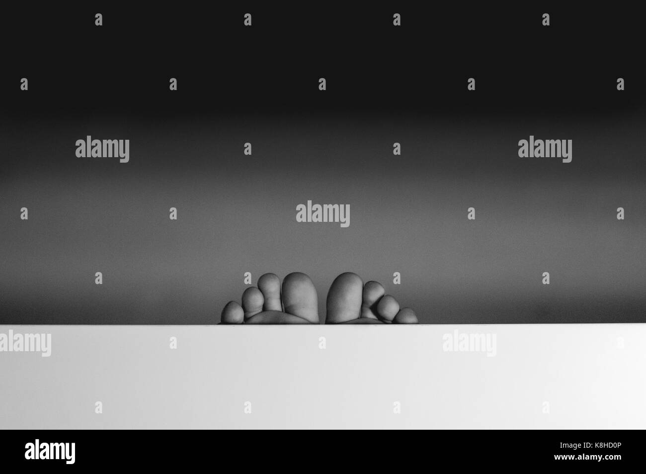 Due piedi stanno emergendo da una superficie bianca in primo piano Foto Stock