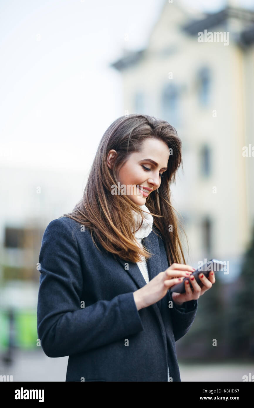 Felice bella donna sulla strada di città con il telefono cellulare la scrittura di sms Foto Stock