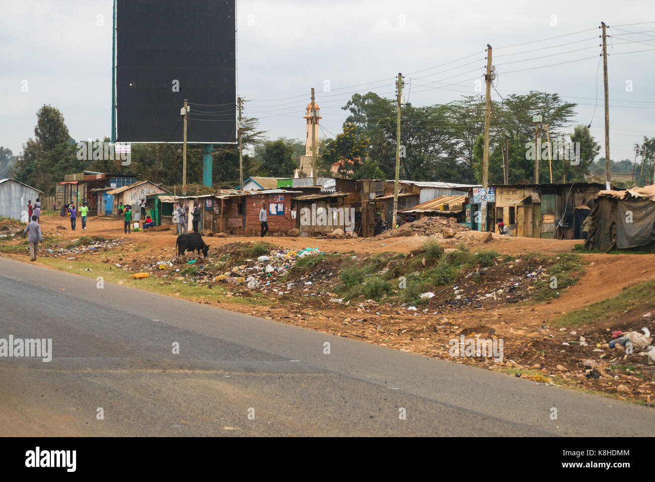 Baracche di strada con la gente e la mucca al di fuori, rifiuti rifiuti linee il piano, Kenya Foto Stock