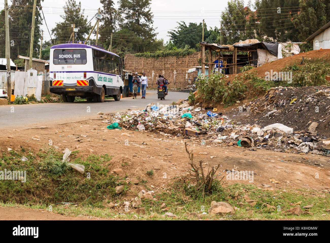 Baracche sul ciglio della strada e il bus di scuola con persone, rifiuti Rifiuti in primo piano, Kenya Foto Stock