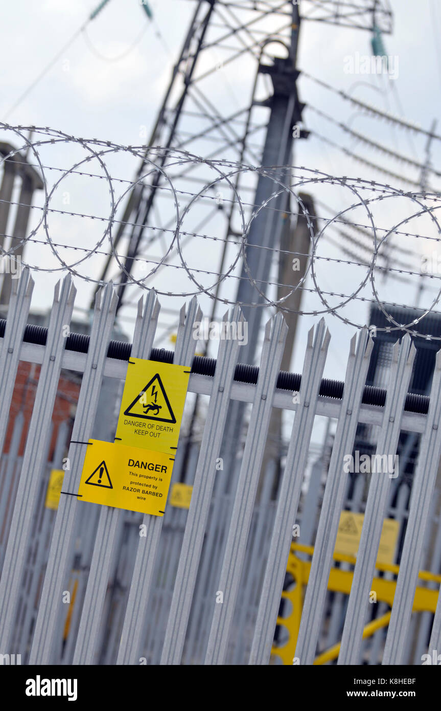 Un consiglio di amministrazione di energia elettrica sotto alla stazione con palizzata scherma e pericolo di morte cartelli gialli attaccato per la scherma come avvisi di intrusi Foto Stock