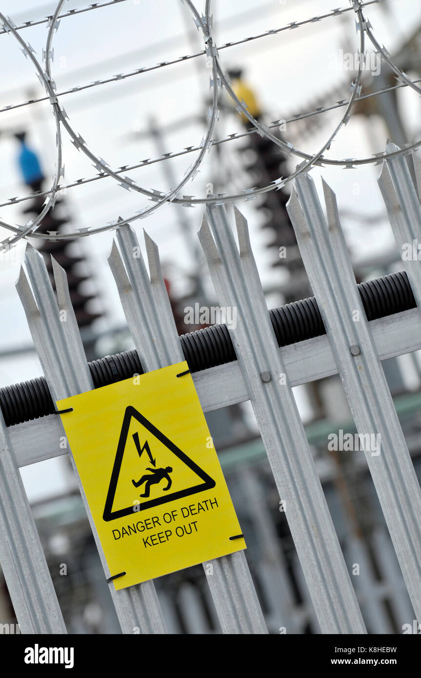 Un consiglio di amministrazione di energia elettrica sotto alla stazione con palizzata scherma e pericolo di morte cartelli gialli attaccato per la scherma come avvisi di intrusi Foto Stock