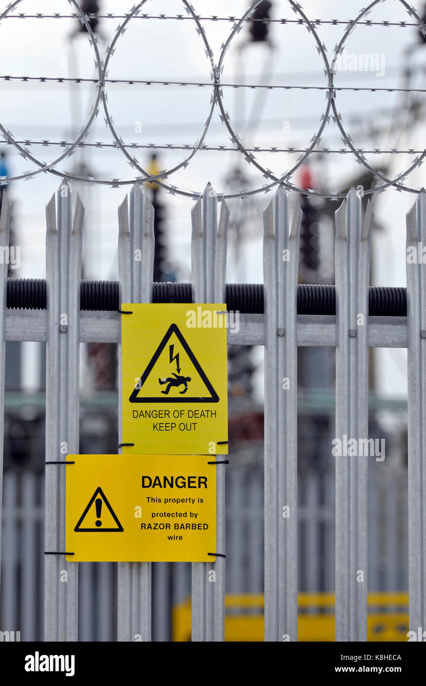 Un consiglio di amministrazione di energia elettrica sotto alla stazione con palizzata scherma e pericolo di morte cartelli gialli attaccato per la scherma come avvisi di intrusi Foto Stock