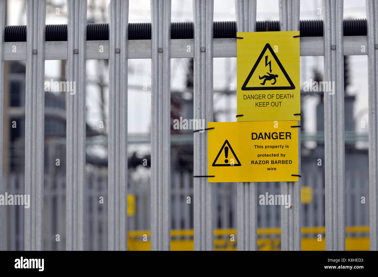 Un consiglio di amministrazione di energia elettrica sotto alla stazione con palizzata scherma e pericolo di morte cartelli gialli attaccato per la scherma come avvisi di intrusi Foto Stock