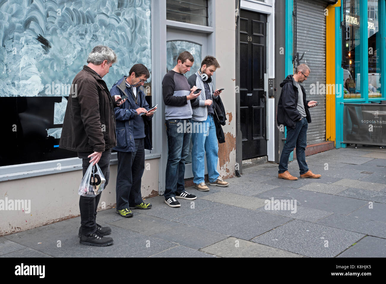 Un gruppo di cinque uomini controllare i loro telefoni cellulari su Lothian Road, Edimburgo, Scozia, Regno Unito Foto Stock